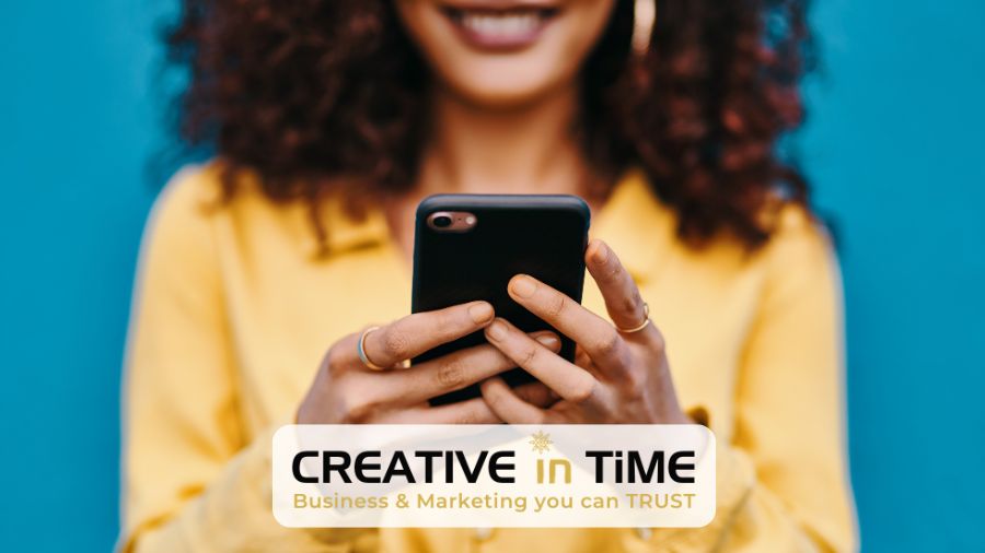 Image of a black lady in a yellow shirt holding a black mobile phone. The logo for CREATIVE in TiME is overlayed in the lower centre of the image.